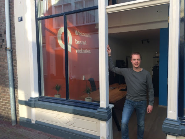 Man staat bij ingang met raamreclame 'WeComm bouwt websites'.