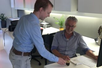 Twee mannen overleggen op kantoor met koffie.