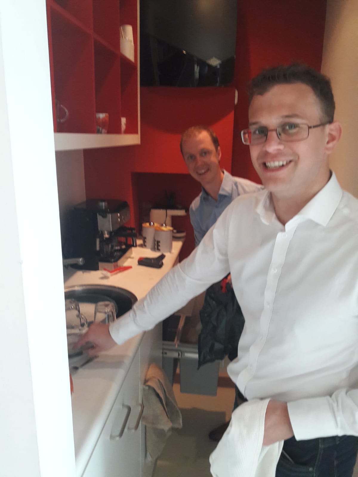 Twee mannen glimlachen in moderne rode keuken.