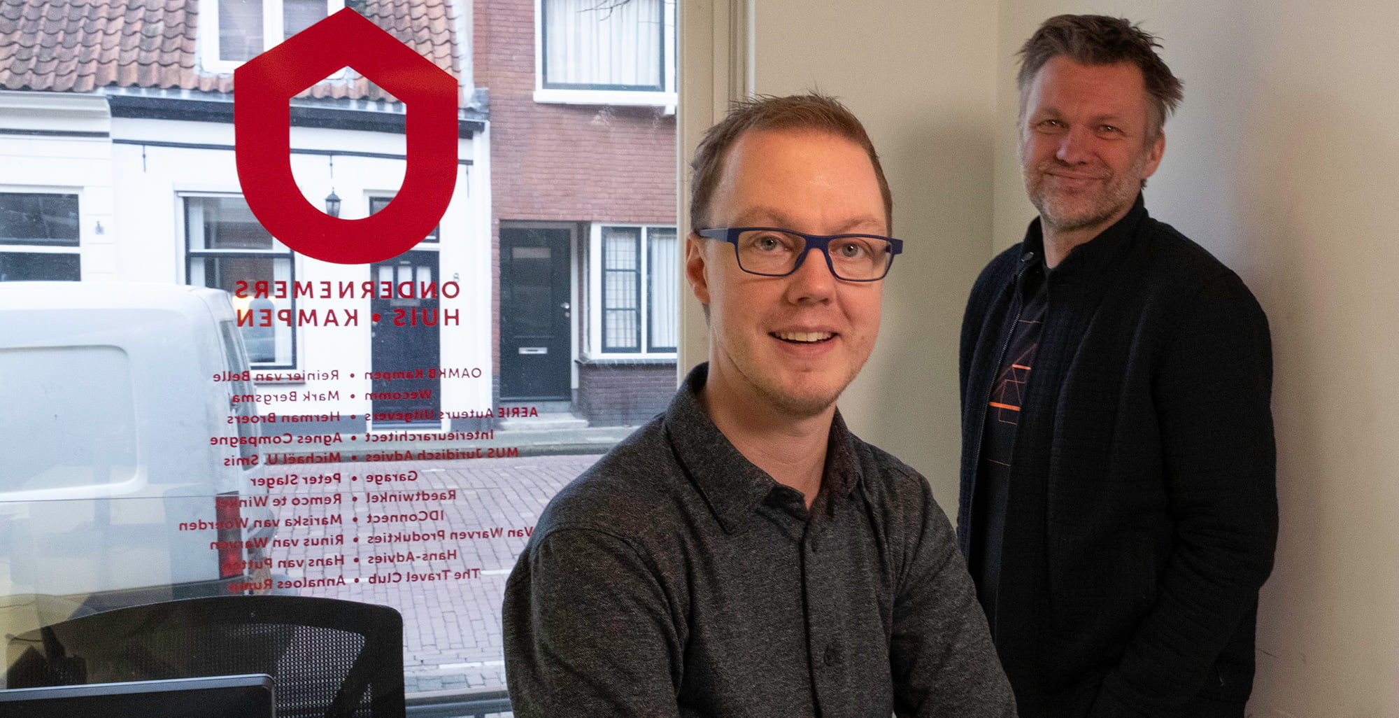 Twee mannen in kantoor met bedrijfslogo op raam.